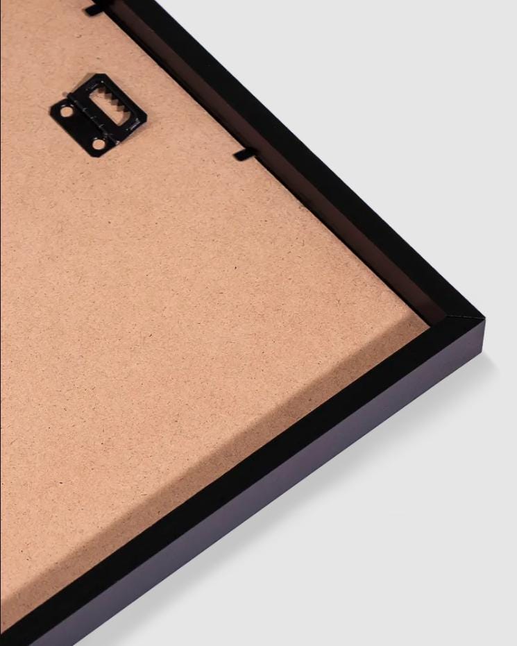 a close-up view of a black-framed picture frame with a piece of cardboard inside it, placed on a white surface.
